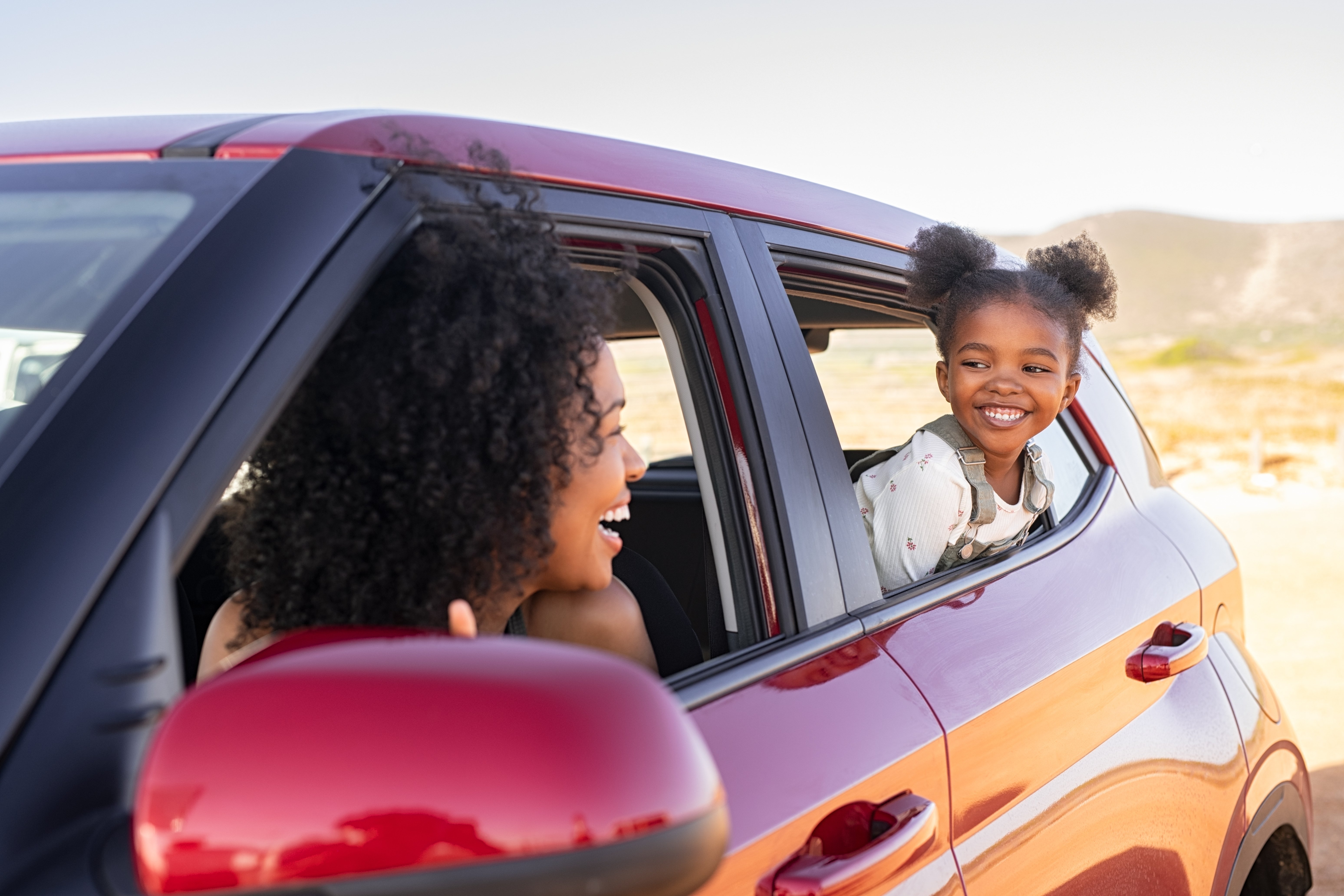 Mother and daughter smiling at each other through the windows of a red SUV.