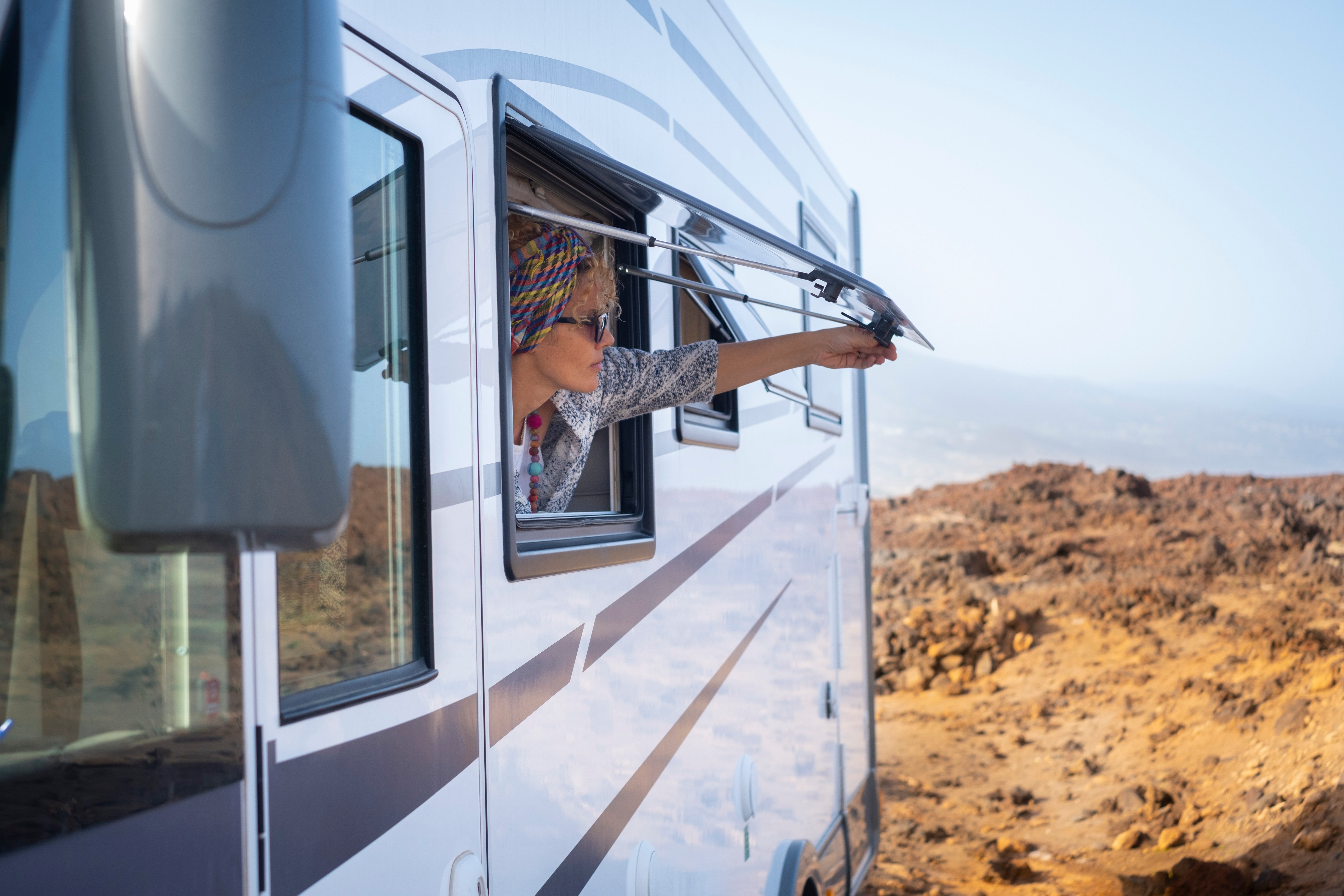 A woman looking out of an RV window in a rocky desert.