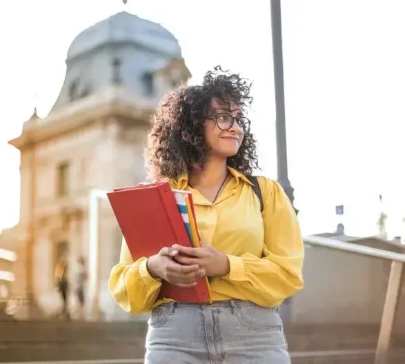 Female college student holding books standing on stairs (1)