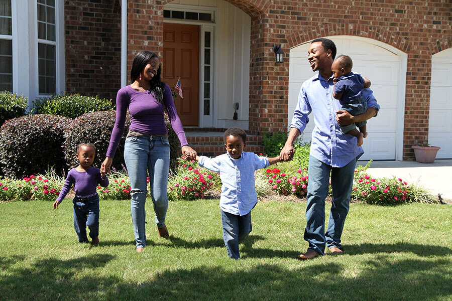 A family smiling outside their home after lowering their mortgage payments with a mortgage refinance.