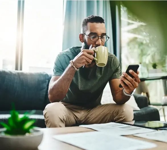 Man sitting on the couch looking at his phone and drinking coffee